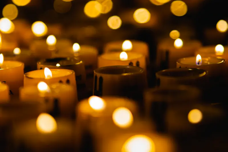 Rows of lit candles glowing with warm bokeh in a dark room