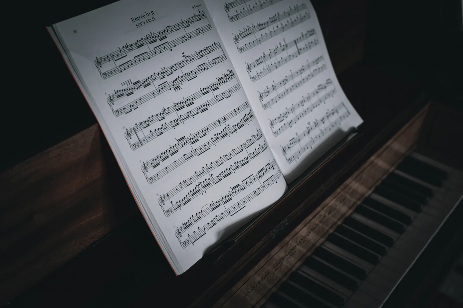 Open book of sheet music resting on an upright piano in low light