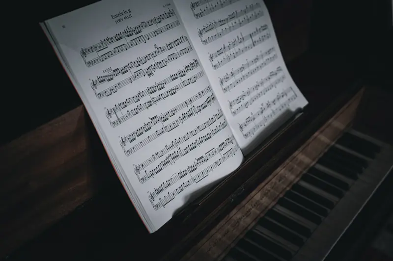 Open book of sheet music resting on an upright piano in low light