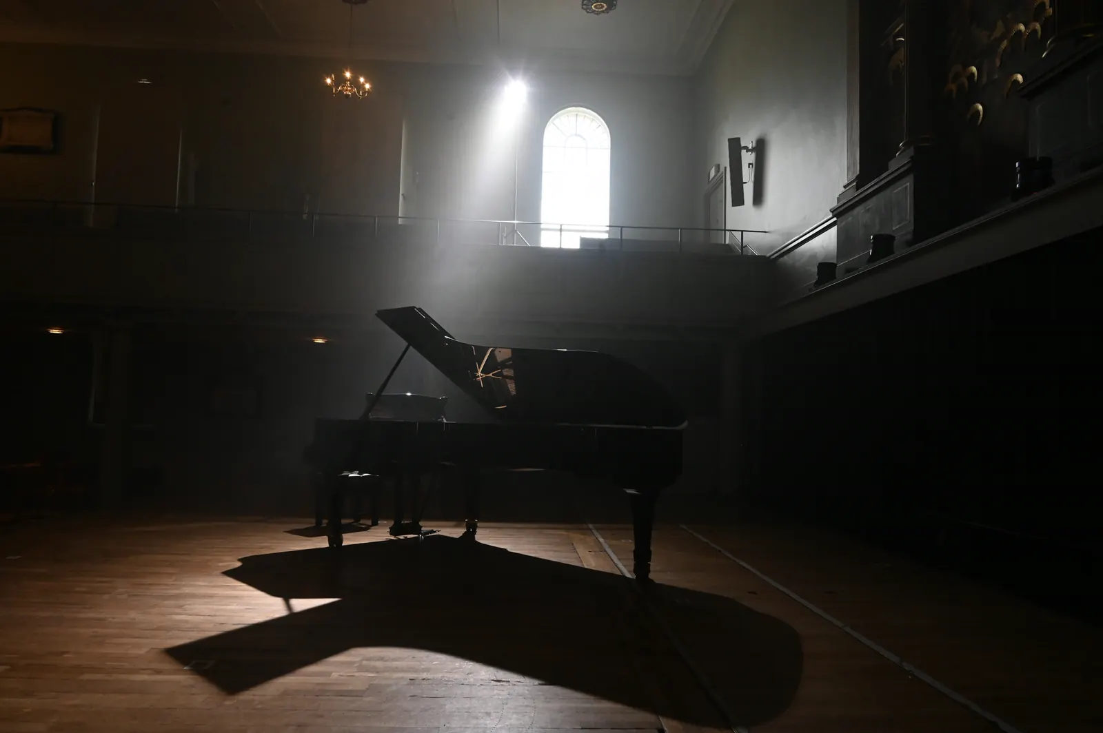 Black grand piano in a dim hall lit by a single shaft of window light