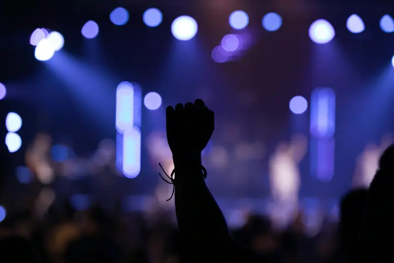 Silhouette of a raised hand during worship under purple and blue stage lights