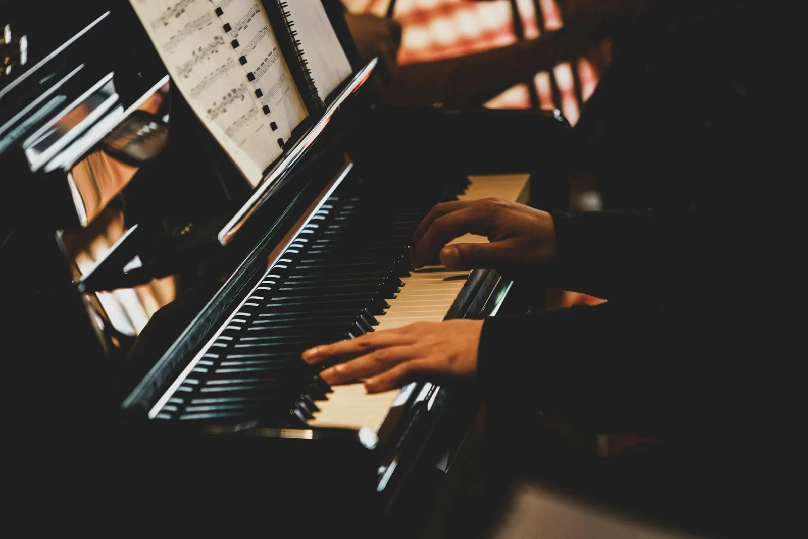 Close-up of hands playing a piano keyboard in a dark room with warm side light