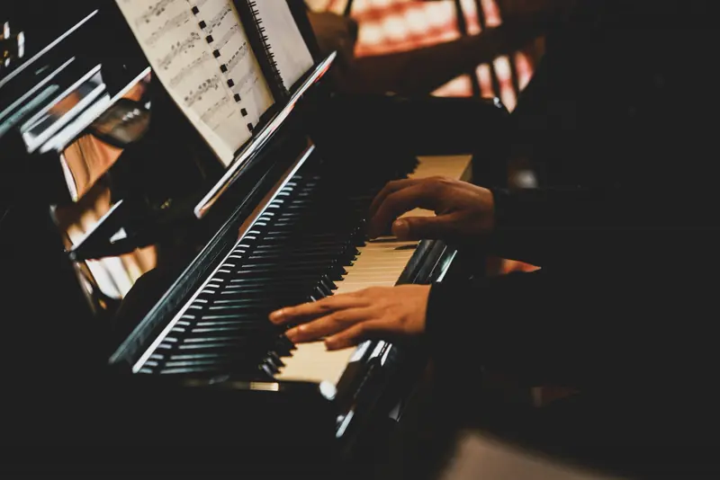Close-up of hands playing a piano keyboard in a dark room with warm side light