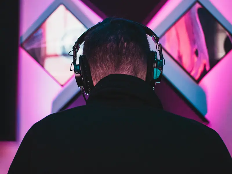 Musician seen from behind wearing studio headphones in a magenta-lit room