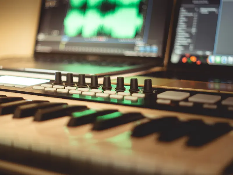 MIDI keyboard controller with knobs and pads in front of a laptop running music software