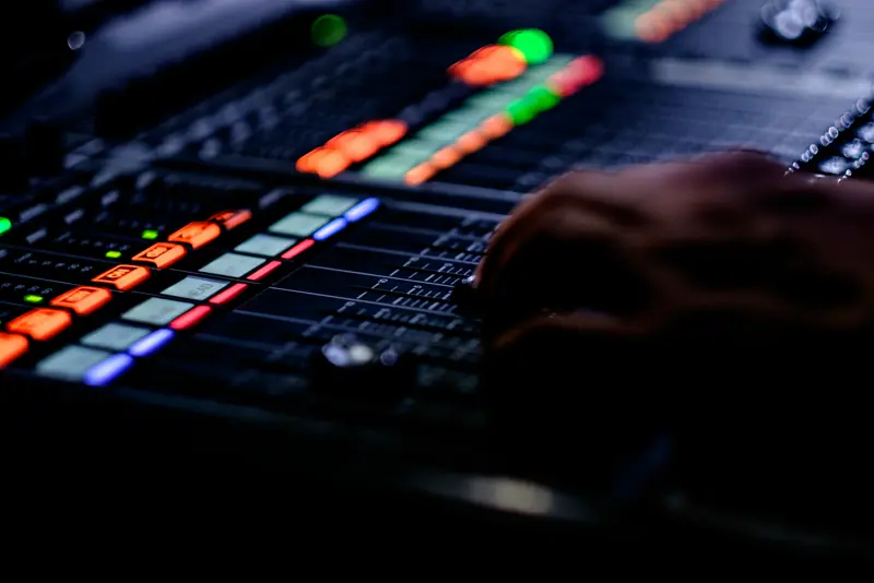 Hand adjusting faders on a sound mixing console with glowing buttons in the dark