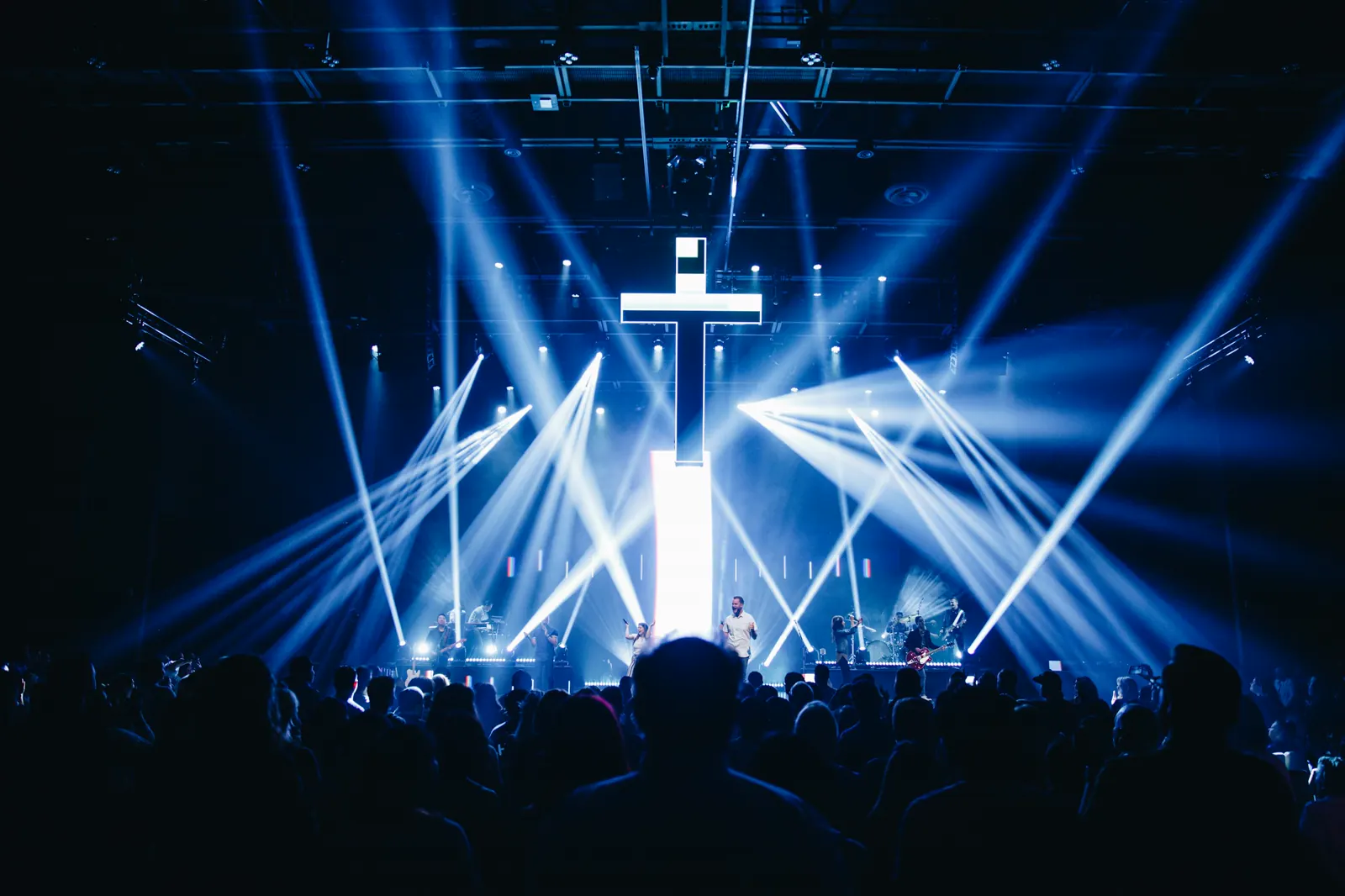 Modern church auditorium with a lit cross, blue beam lights and a worship band on stage