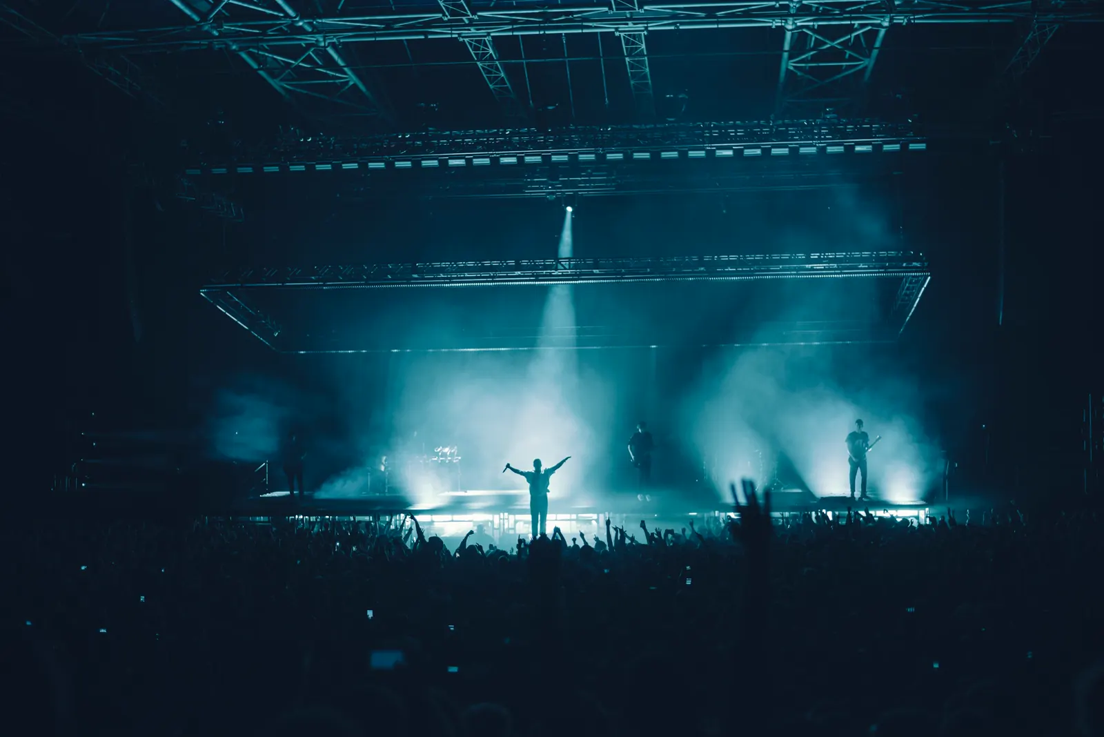 Silhouetted performer on a hazy concert stage under teal spotlights above a crowd